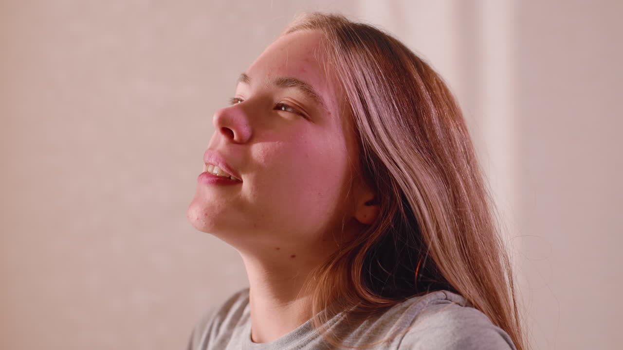 Close up side view of housewife with eyes closed stretching arms behind head after restful sleep in cozy room, soft warm light streaming through curtain illuminating calm relaxed face