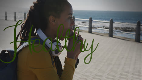 una pancarta de texto saludable contra una mujer afroamericana que come un bocadillo en el paseo marítimo