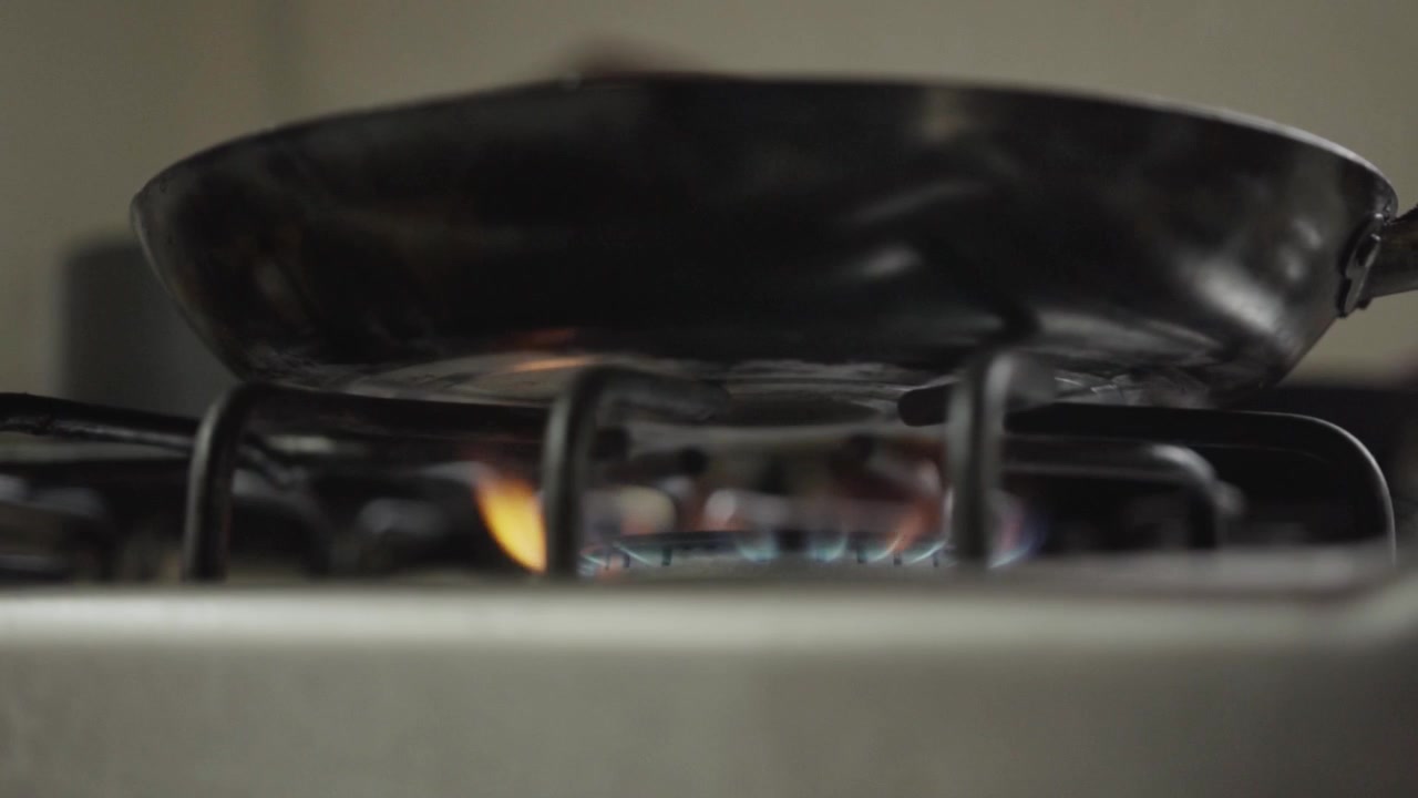 Padella vuota che si scalda sopra un fornello a gas attivo con fiamma blu visibile in un ambiente cucina.