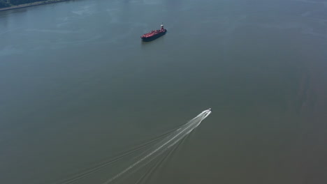 a drone view of a large red barge anchored and a small boat going by in the hudson river in ny on a sunny day