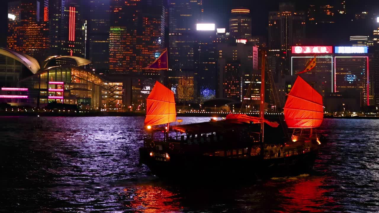 A vibrant red-sailed junk boat glides across the water, reflecting city lights from towering skyscrapers.