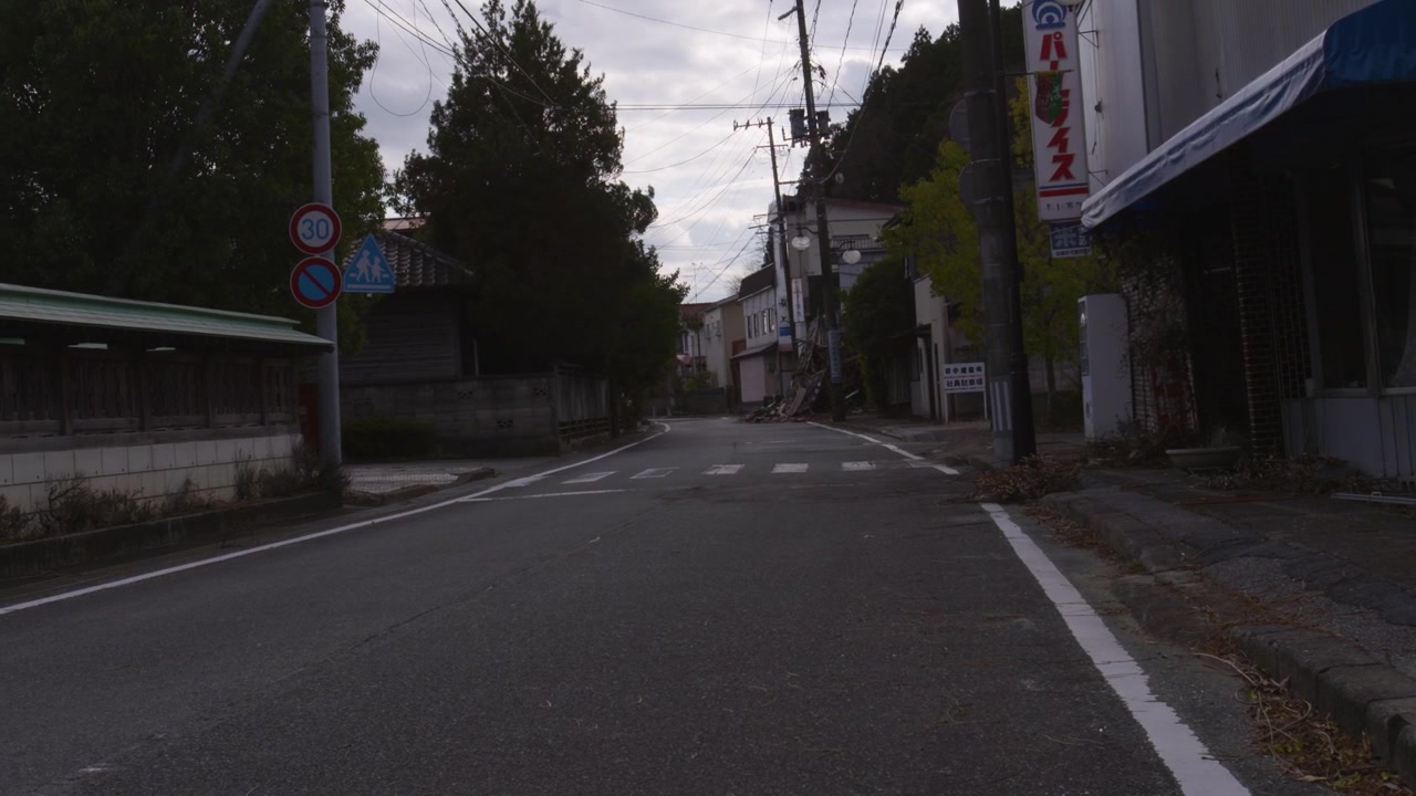 Statisk billede af en stille, tom gade i en japansk by under en overskyet himmel.