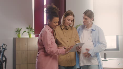 three pregnant woman looking at tablet and talking in the office 1