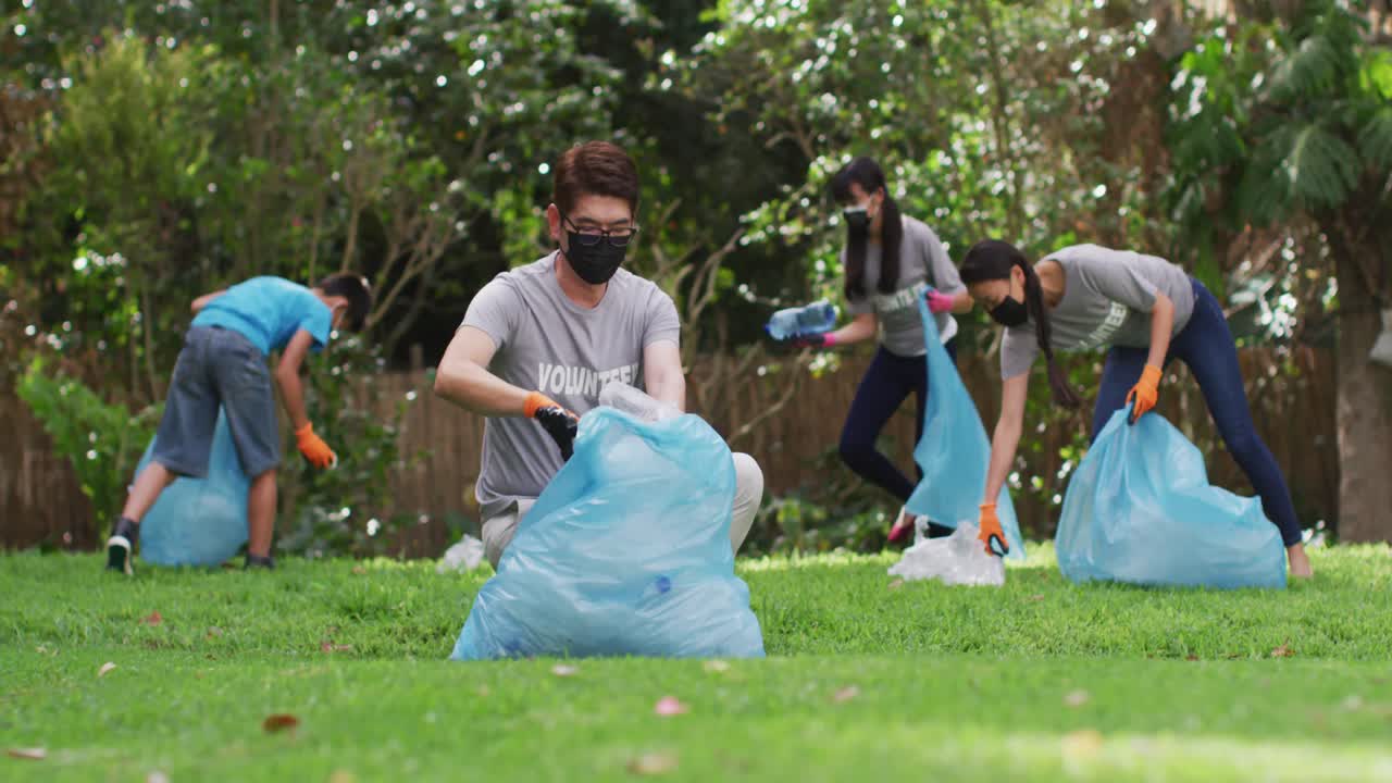 Genitori, figlio e figlia asiatici che indossano mascherine, che tengono sacchi per i rifiuti e raccolgono rifiuti di plastica.