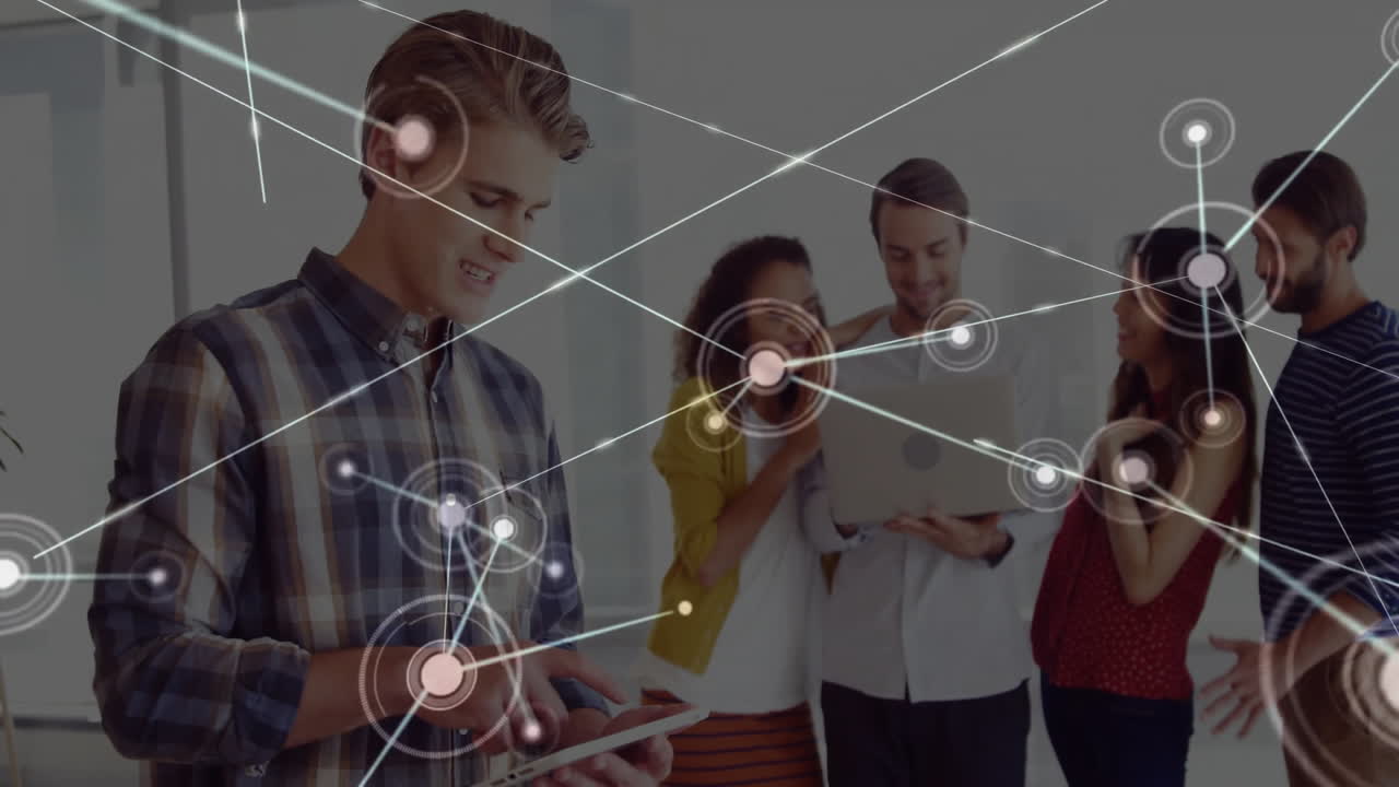 Man tapping tablet in modern office, tech team collaborating around laptop with data nodes graphic