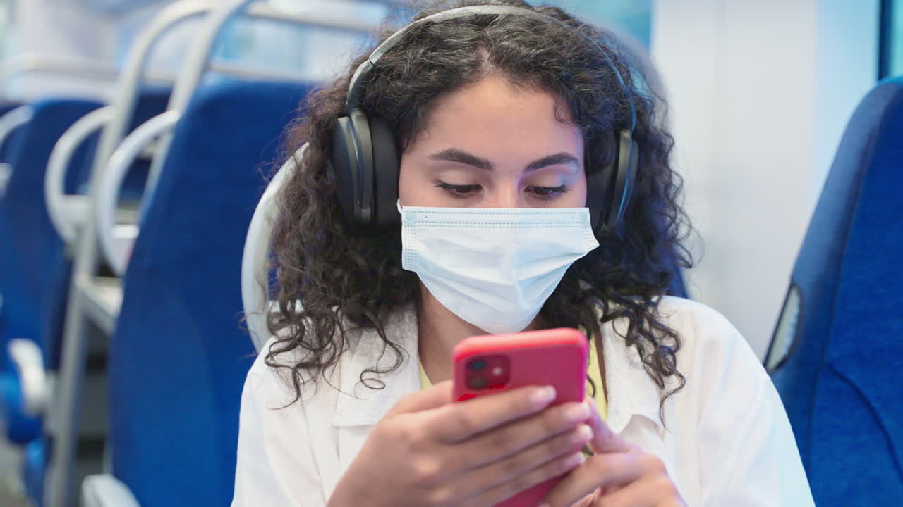 mujer usando el teléfono en un tren usando una máscara y auriculares