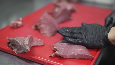 chef, con guantes negros cortando hábilmente carne leída en una tabla de cortar roja