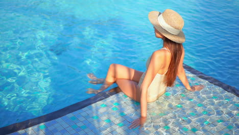 Mujer-Atractiva-En-Traje-De-Baño-Y-Sombrero-Sentado-En-La-Piscina-Azul-En-Un-Día-Soleado