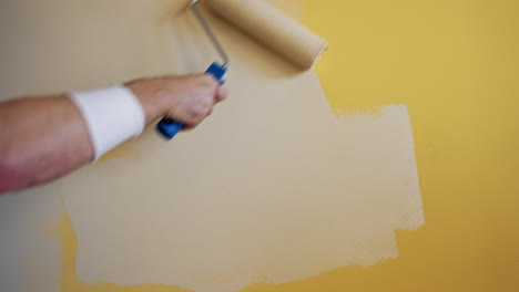 roller painting yellow wall with creamy paint. hand of a worker doing renovation the room with light color. close-up. makeover concept.