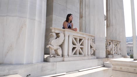 shot of a young asian woman who leans on a balcony of an old marble building in athen