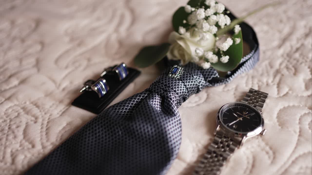 Close up of a tie with cufflinks boutonniere and watch laid out on a decorative bedspread