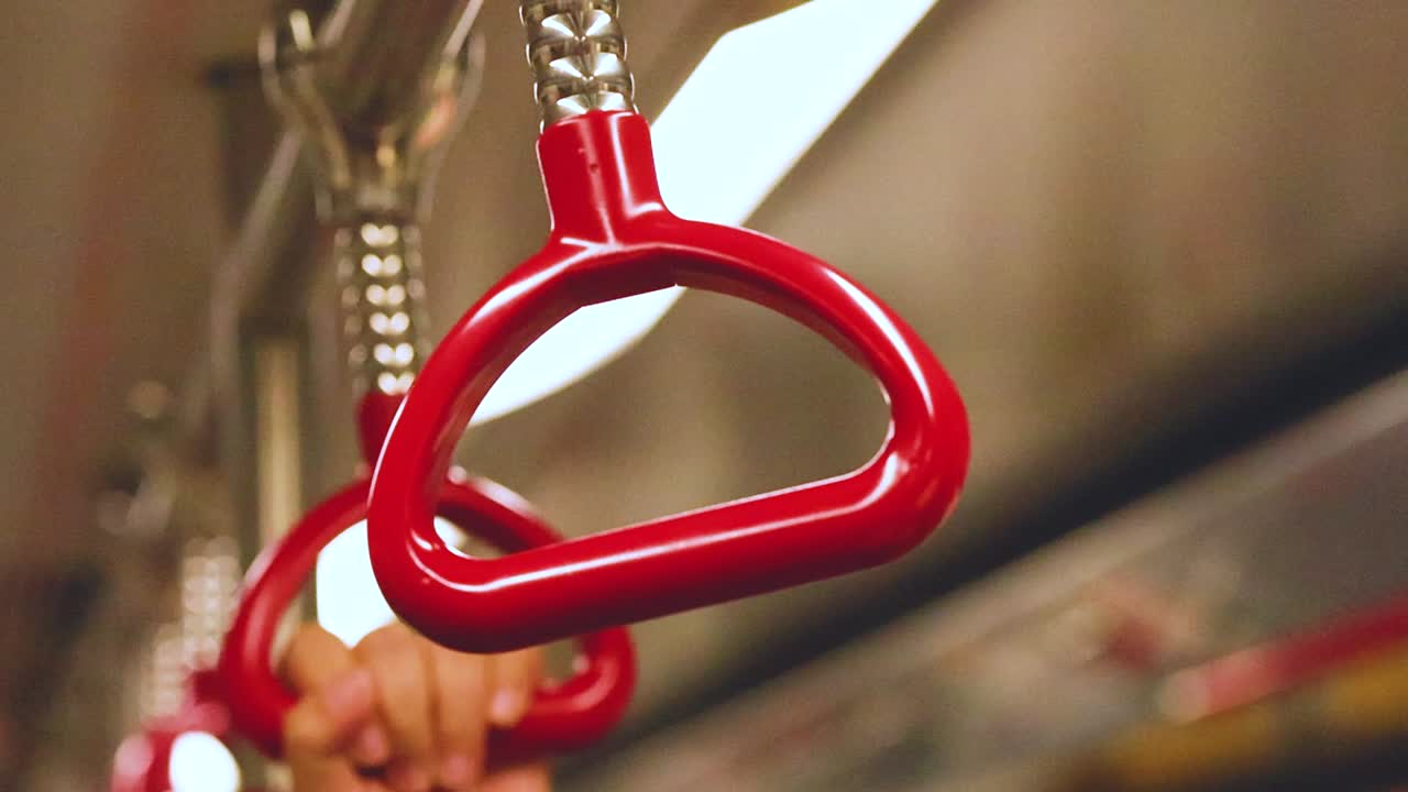 Close-up of hands holding red handles on a moving train, emphasizing stability and grip.