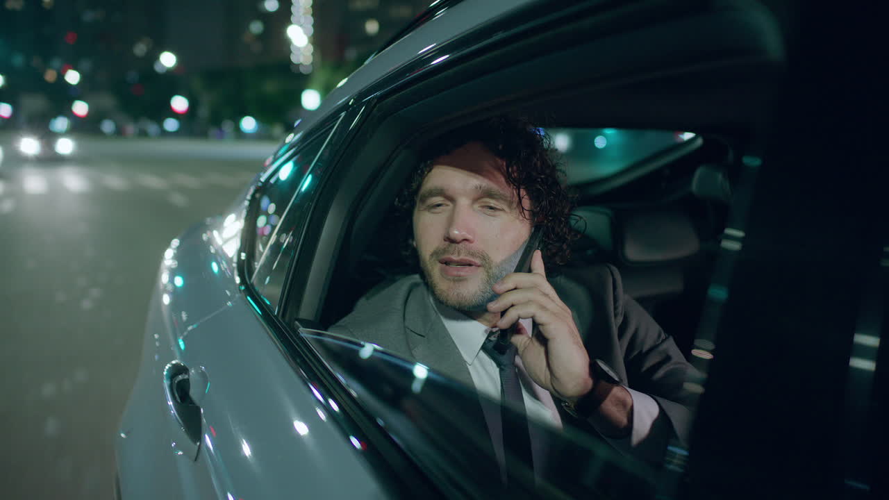 Businessman Having Phone Conversation during Taxi Ride through Night City