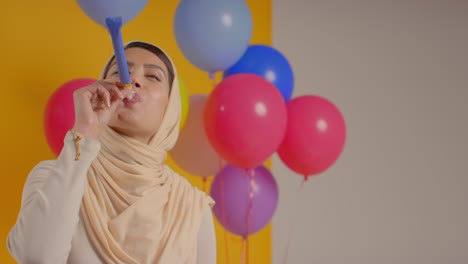 studio portrait of woman wearing hijab celebrating birthday with balloons and party blower 1