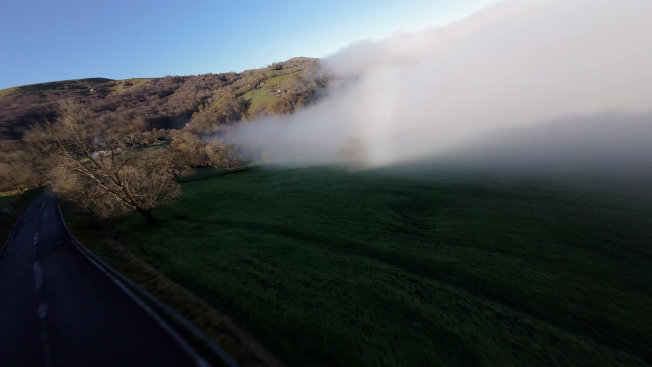 FPV drone descends into thick fog blanketing a mountain valley. Captured in Vega de Pas, Northern Spain, on a sunny winter morning.