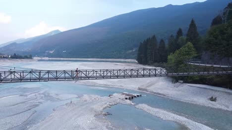 person passing on bridge over barcis lake in italy alps, aerial orbit view