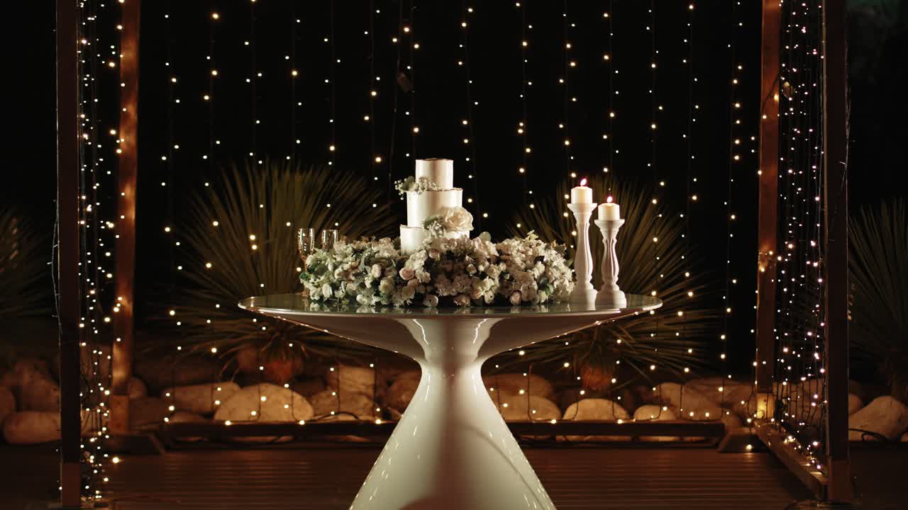 romantic wedding cake display with flowers and candles lit by soft string lights