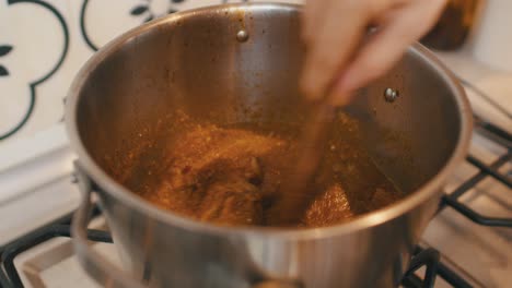 chef stirs mixture of potato, meat and vegetables topped with sauce inside hot cooking pot on a stove