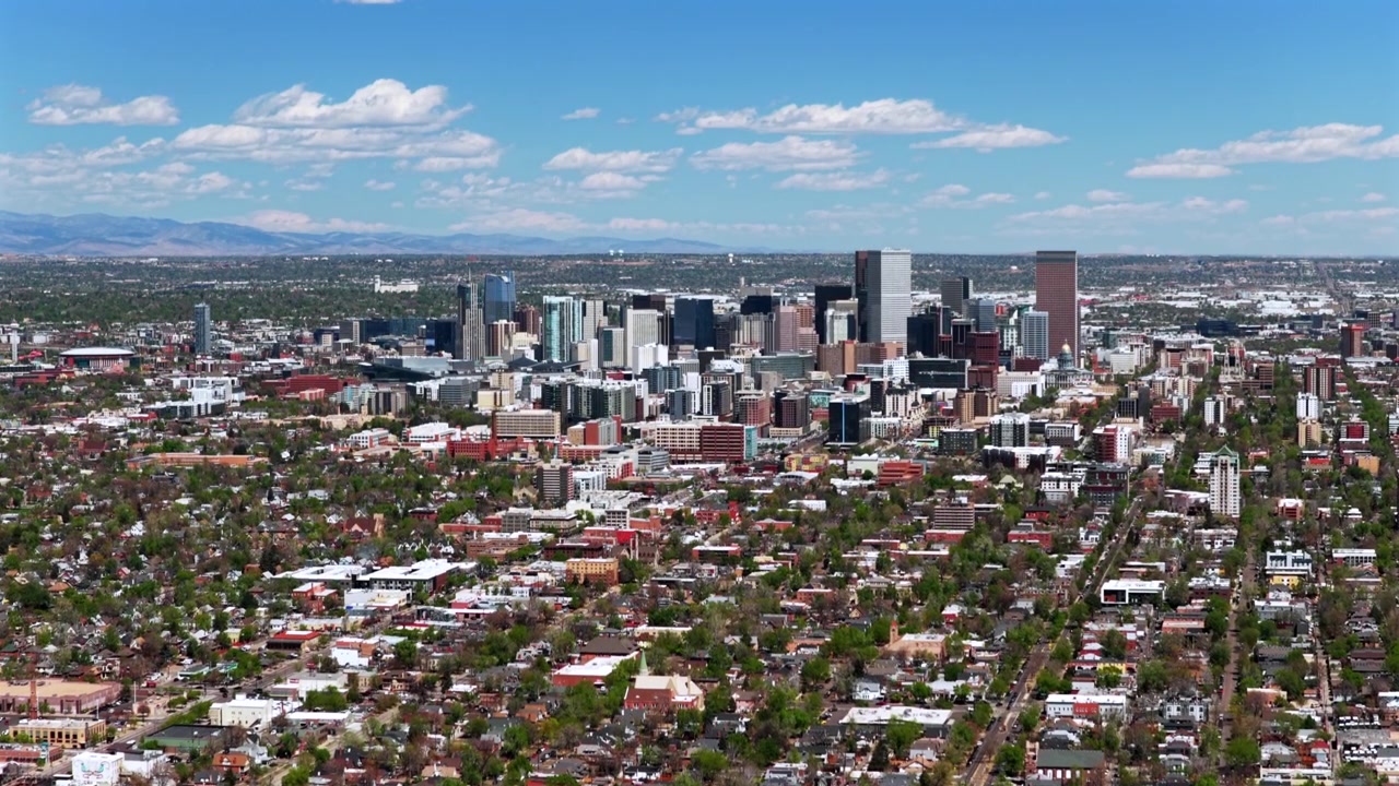 Downtown Denver om foråret/sommeren en solrig morgen, med skyskrabere i Lodo og Capitol Hill. Luftfoto med drone af Colorados bybillede og landskab, der viser City Park-kvarteret og Front Range Rockies, med en fremadgående panorering opad.