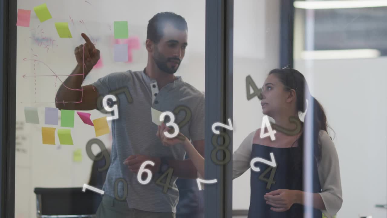 Coworkers picking up sticky note, annotating business graph on glass and placing note as data swirl
