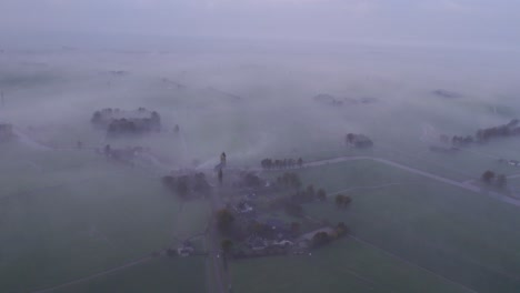 Wide-shot-of-Kerk-van-Hichtum-with-low-fog-during-sunrise,-aerial