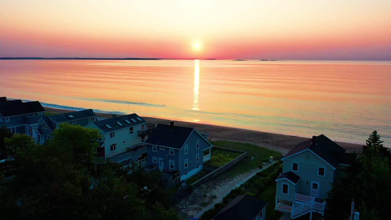해가 지는 색은 해변에 있는 집들을 내려다보는 바다의 파도에서 반사됩니다.