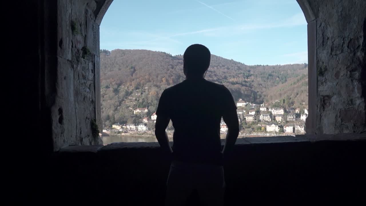 Silhouette of a man standing in front of an ancient window of a castle overlooking a colorful German town.