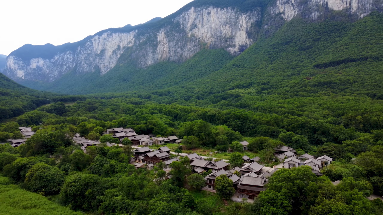 Aerial Mountain Village Nestled In Lush Green Forest Beneath Towering Limestone Cliffs Traditional Wooden