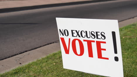 Campaign-Voter-Rally-Sign-Next-to-Road-with-Cars-Driving-By-Close-Up,-No-Excuses-Vote