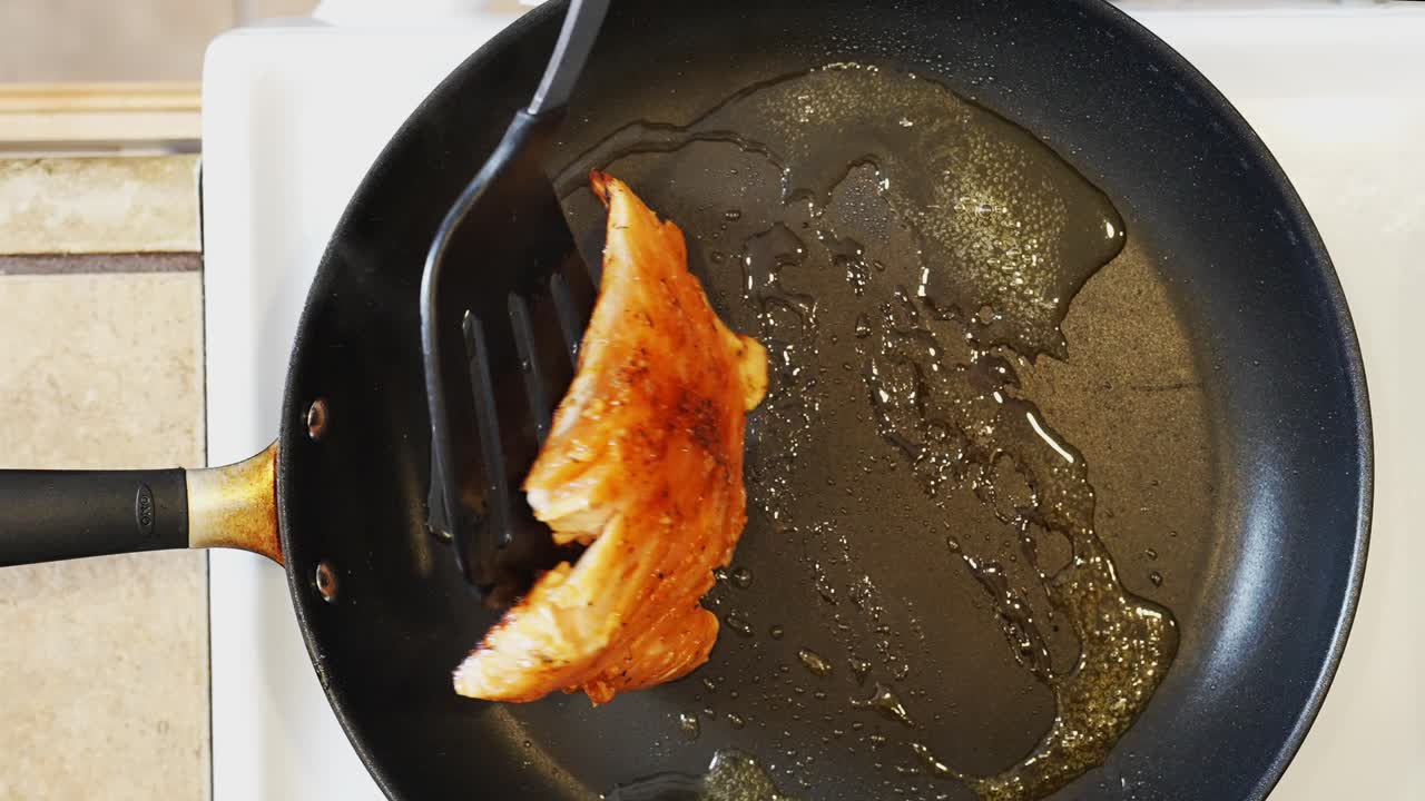 Vender en laksefilet på en stegepande på komfuret, mens den syder i varm vegetabilsk olie - set ovenfra
