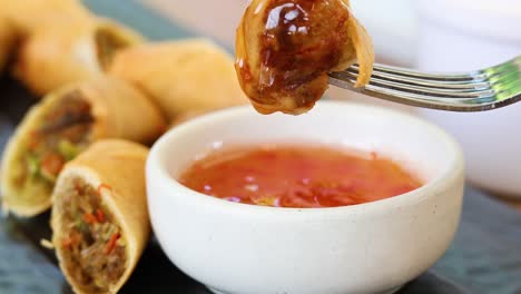 spring roll being dipped into sweet chili sauce