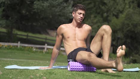 4K-Young-caucasian-fit-attractive-male-exersicing-outdoors-with-green-vegetation-background-Foam-roller-upper-legs-on-calves-exercise