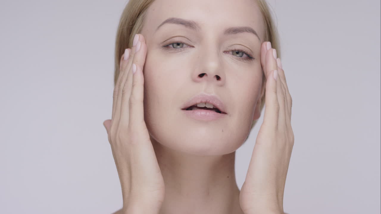 아름다운 건강한 여성이 회색 배경에 아름다움 피부 관리 개념을 위해 느린 움직임으로 얼굴에 부드러운 피부를 만지고 빨간 서사시 드래곤