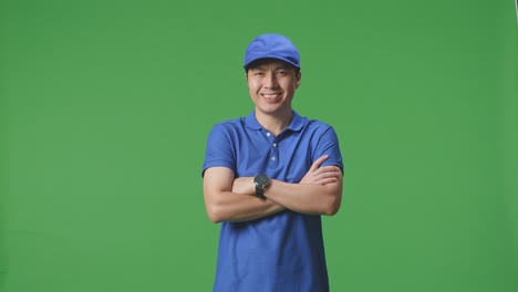 mensajero masculino asiático en uniforme azul sonriendo cruzando los brazos en el fondo de la pantalla verde en el estudio