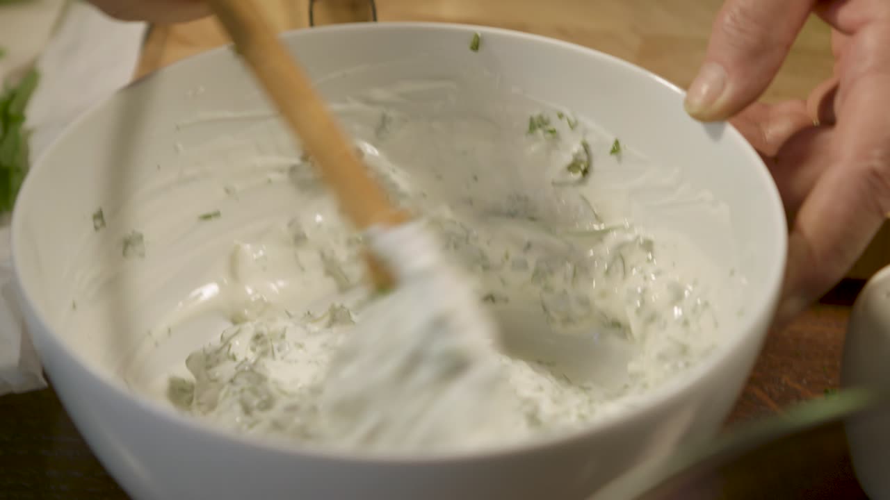 Mixing fresh herb yogurt sauce with a wooden spoon in a white bowl