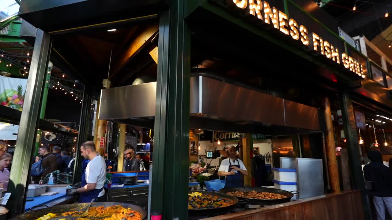 Paella vendor serving large pans of colorful paella to market visitors at London's Borough Market
