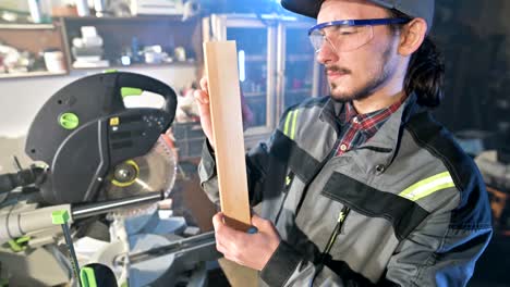 concentrated young bearded joiner in goggles and a cap checks the work piece