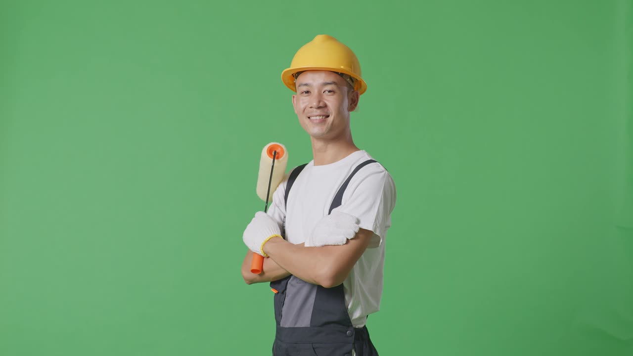 Side View Of Asian Man Painter Wearing Safety Helmet Smiling And Crossing His Arms While Standing In The Green Screen Background Studio