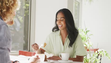 Happy-diverse-couple-eating-cake-and-talking-at-a-table-in-cafe