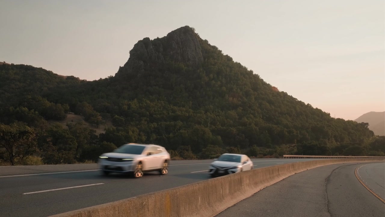 Vehículos circulan por la Autopista 152 con una montaña escarpada elevándose al fondo bajo un cielo abierto y brillante.