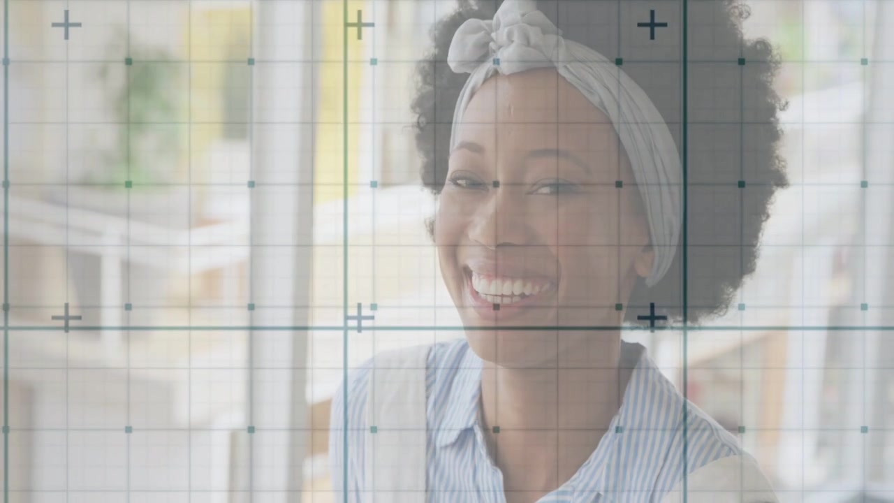 African American woman using stylus on tablet at desk, wearing striped shirt and apron, smiling up