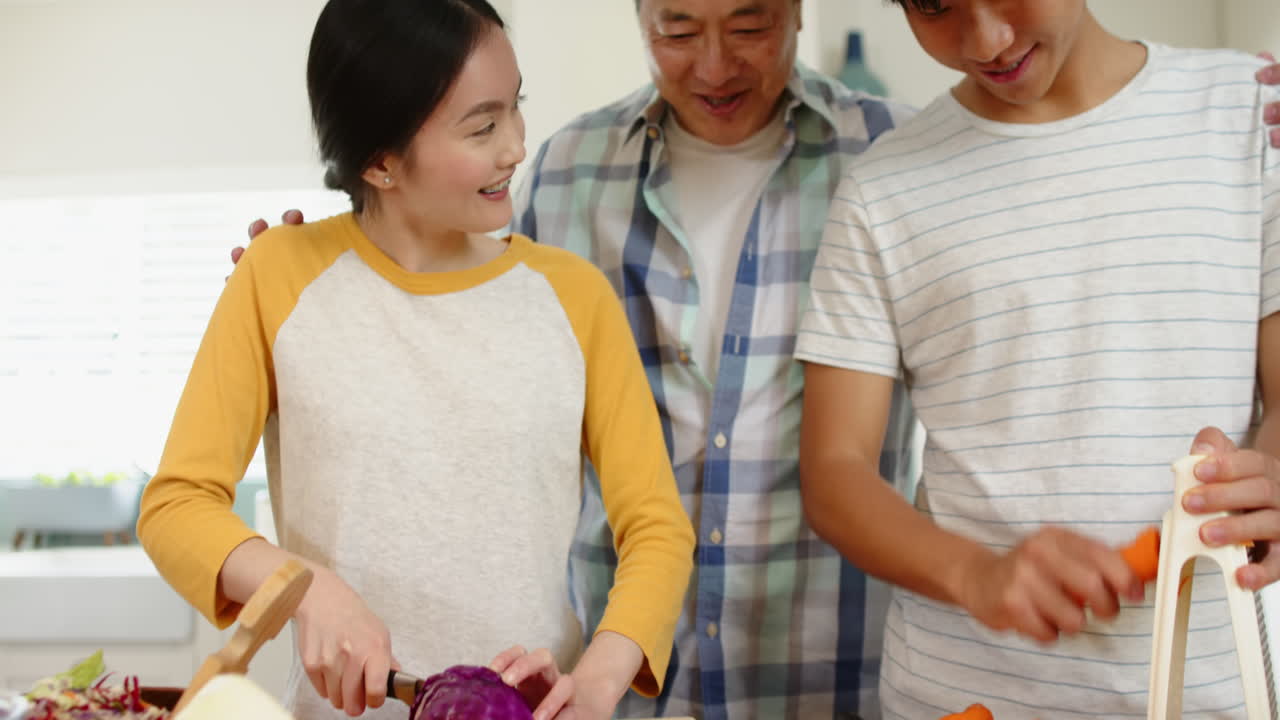 Family preparing vegetables together, chopping cabbage and carrots in kitchen