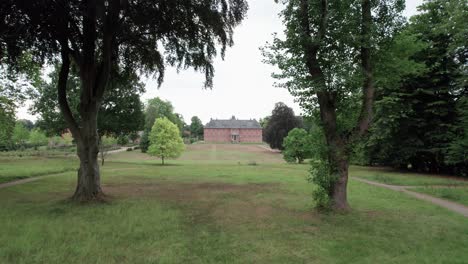4k aerial drone fly through branches and trees revealing an old historical castle of denmark on green fields and lush garden on a summer day
