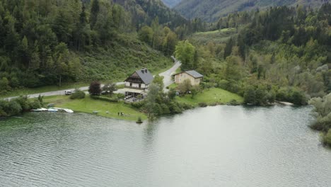 Orilla-Sur-De-La-Presa-Del-Embalse-De-Freibach-En-Austria-Con-Restaurante-Griego-Stausewirt-Y-Cabaña-Con-Gente-A-La-Izquierda,-Vista-De-Avance-De-La-órbita-Aérea