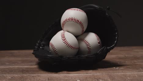 Cerrar-Estudio-De-Béisbol-Bodegón-Con-Pelotas-En-El-Guante-Del-Receptor-En-El-Piso-De-Madera-3