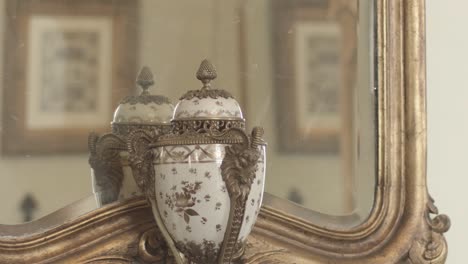 close up of vase with delicate ornaments in front of ancient mirror with 18th century frame