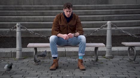 joven esperando en un banco de la ciudad, molesto, revisando su reloj