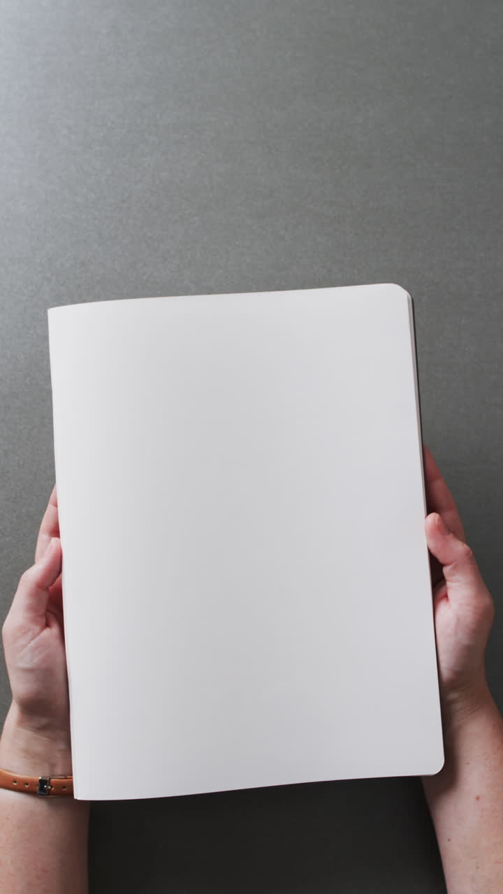 Vertical video of hand holding book with copy space on gray background in slow motion