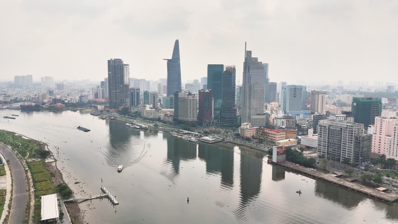 Vietnam, Ho Chi Minh Şehri şehir merkezinin havadan görünümü; Saygon Nehri'ne yansıyan modern gökdelenler, sakin suda ilerleyen tekneler ve sahil şeridini çevreleyen kentsel altyapı