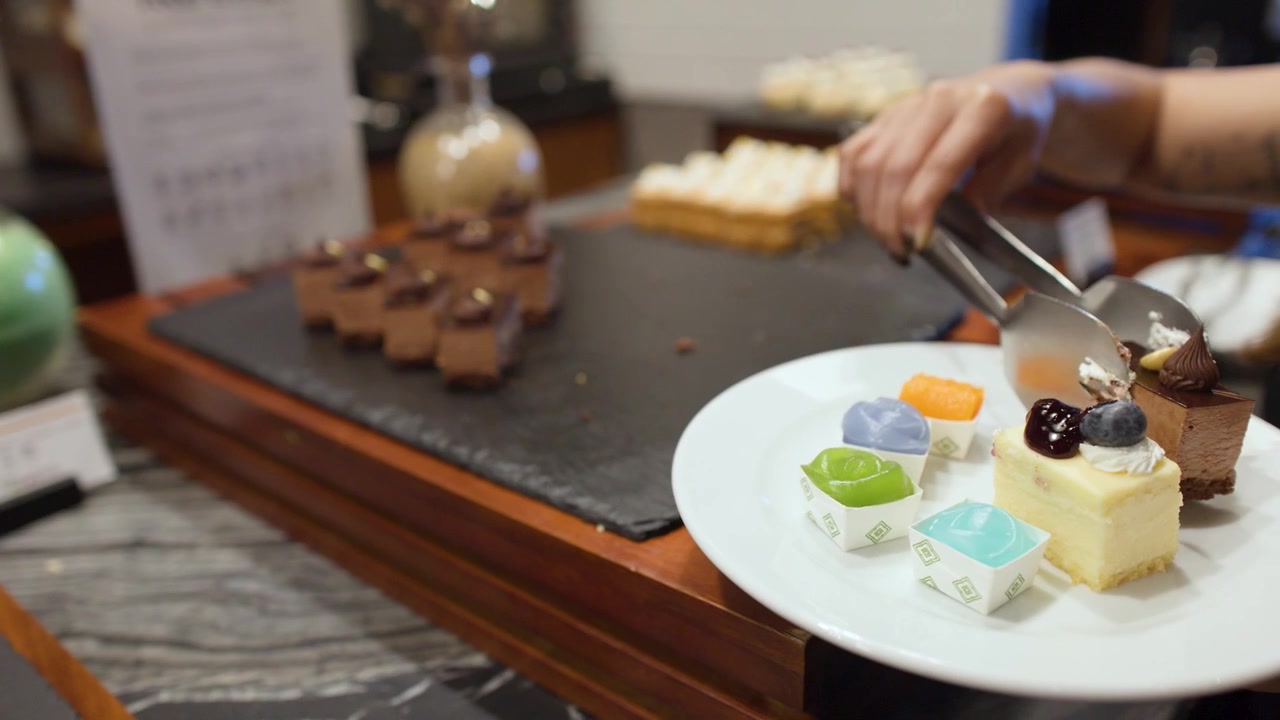 A hand uses metal tongs to transfer chocolate mousse cake onto a white dessert plate